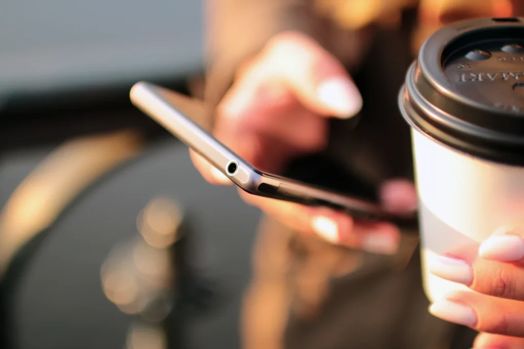 Akıllı telefon ve siyah kapaklı karton bardak tutan eller.