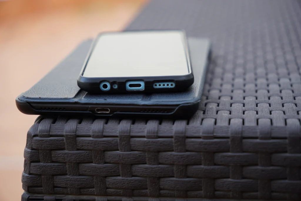 Koyu renk örgülü masa üzerinde, kılıflı bir tabletin üstüne yerleştirilmiş akıllı telefon.